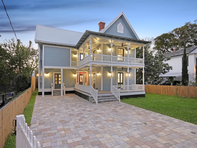 view of front of home featuring metal roof, a porch, fence private yard, a balcony, and a front yard