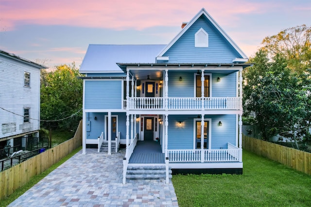 rear view of property featuring french doors, covered porch, a lawn, fence, and a balcony