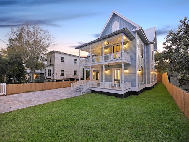 back of property at dusk featuring a lawn, fence private yard, a balcony, and a ceiling fan