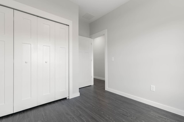 unfurnished bedroom featuring baseboards, dark wood-style flooring, and a closet