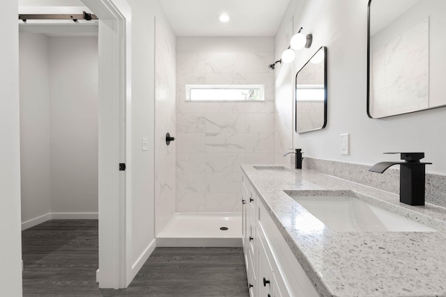 full bath featuring tiled shower, double vanity, recessed lighting, and wood finished floors