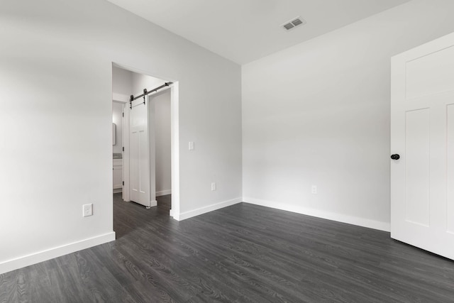 unfurnished room featuring dark wood-type flooring, a barn door, and baseboards