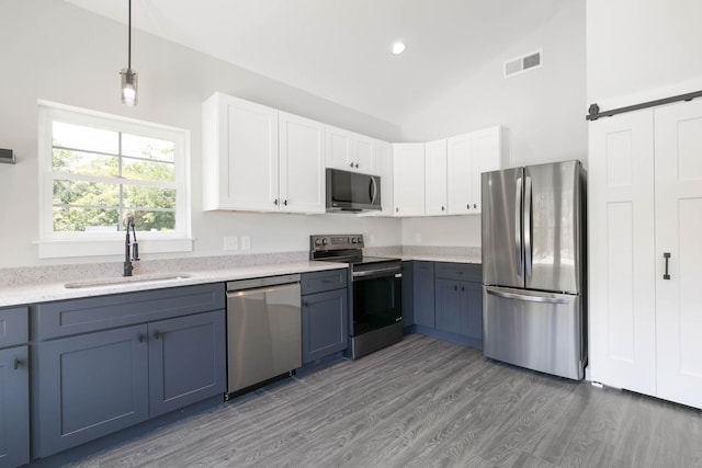 kitchen featuring appliances with stainless steel finishes, a sink, lofted ceiling, light wood finished floors, and white cabinetry