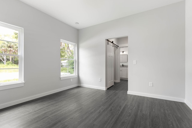 unfurnished bedroom featuring a barn door, dark wood-style floors, baseboards, and ensuite bath