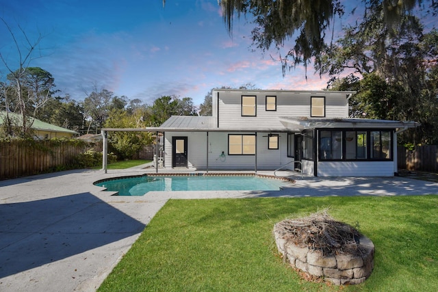 back house at dusk with a patio, a fire pit, a yard, a fenced in pool, and a sunroom