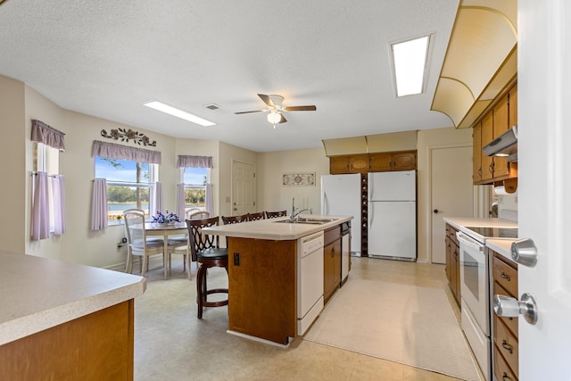 kitchen with a textured ceiling, white appliances, ceiling fan, sink, and a center island with sink