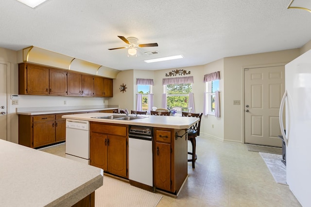 kitchen with white appliances, a center island with sink, sink, ceiling fan, and a textured ceiling