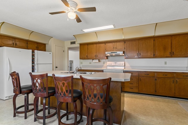 kitchen featuring a breakfast bar, a textured ceiling, white appliances, sink, and a center island with sink