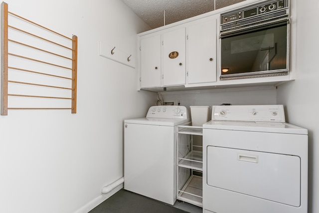 washroom with washer and dryer, a textured ceiling, and cabinets