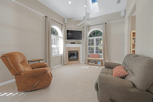 carpeted living room featuring ceiling fan, a tile fireplace, and a skylight