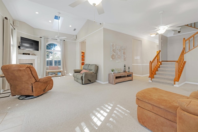 carpeted living room featuring vaulted ceiling with skylight, ceiling fan, and a fireplace