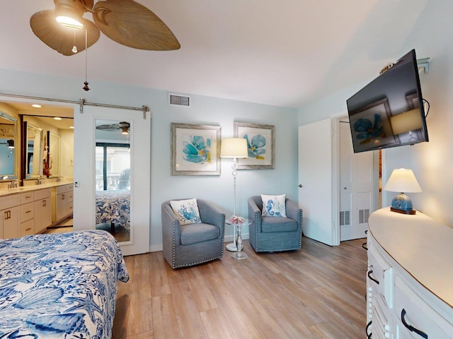 bedroom featuring ensuite bath, ceiling fan, light hardwood / wood-style flooring, and a barn door