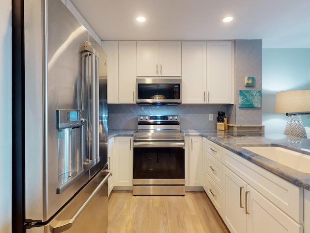 kitchen featuring light stone countertops, appliances with stainless steel finishes, tasteful backsplash, light hardwood / wood-style floors, and white cabinetry