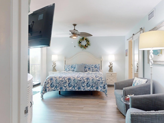 bedroom featuring a barn door, light hardwood / wood-style flooring, and ceiling fan