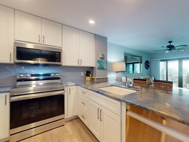 kitchen featuring dark stone counters, sink, light wood-type flooring, appliances with stainless steel finishes, and white cabinetry