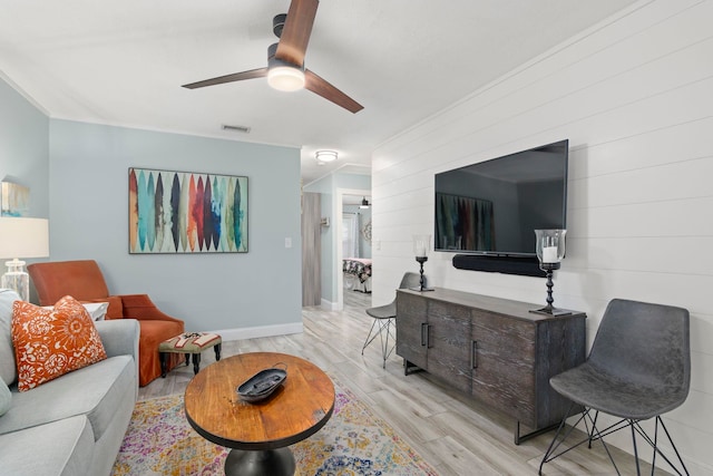 living room with visible vents, crown molding, light wood finished floors, baseboards, and ceiling fan