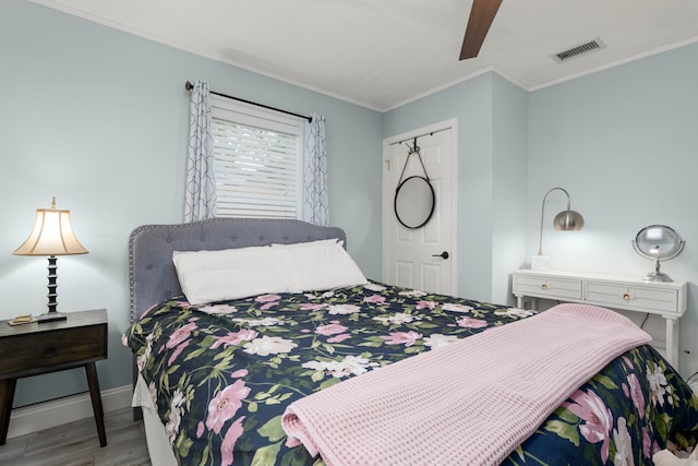 bedroom with wood finished floors, visible vents, baseboards, ceiling fan, and ornamental molding