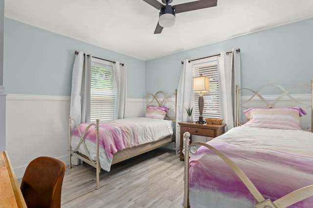 bedroom featuring a ceiling fan, light wood-style flooring, and wainscoting