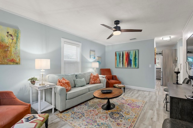 living room with visible vents, crown molding, baseboards, light wood-style floors, and a ceiling fan