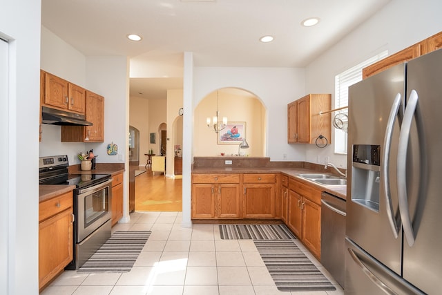 kitchen featuring under cabinet range hood, appliances with stainless steel finishes, arched walkways, light tile patterned flooring, and a sink