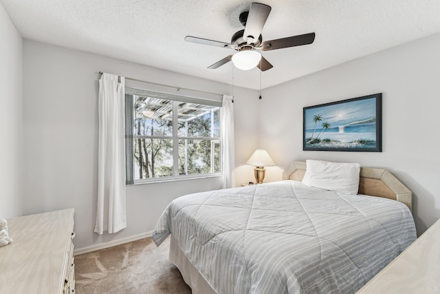 bedroom with ceiling fan, baseboards, a textured ceiling, and light colored carpet