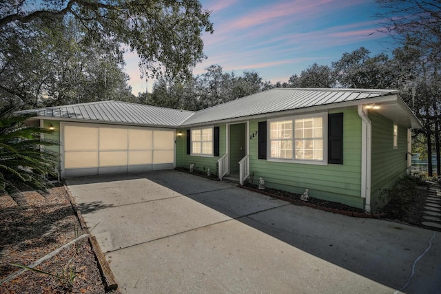 view of front facade featuring entry steps, concrete driveway, metal roof, and an attached garage