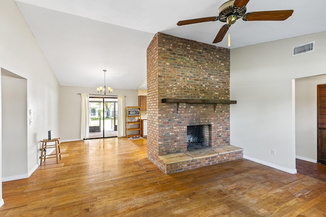 unfurnished living room with baseboards, visible vents, ceiling fan with notable chandelier, a fireplace, and wood-type flooring