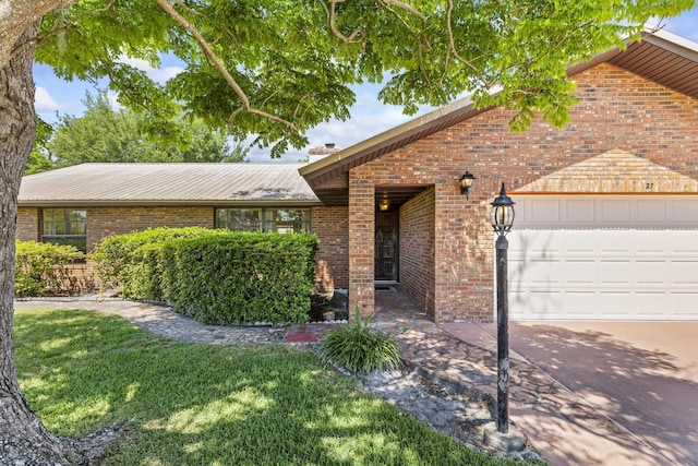 view of front facade featuring metal roof, brick siding, a front yard, and a garage