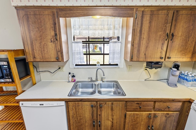 kitchen with white dishwasher, light countertops, brown cabinetry, and a sink