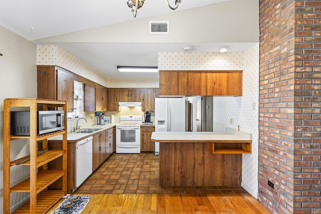 kitchen with vaulted ceiling, visible vents, a sink, white appliances, and a peninsula