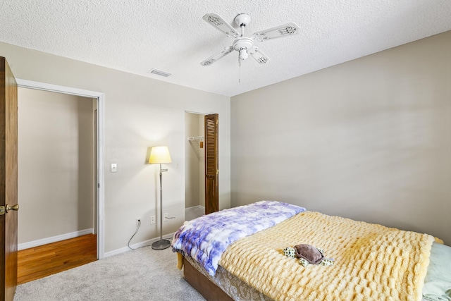 carpeted bedroom featuring a textured ceiling, a closet, ceiling fan, baseboards, and visible vents