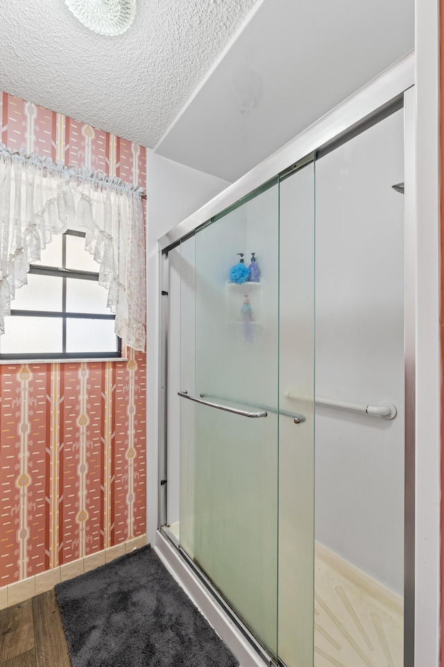 full bathroom with wood finished floors, a shower with shower door, and a textured ceiling
