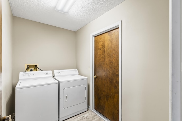 clothes washing area featuring a textured ceiling, light wood finished floors, separate washer and dryer, and laundry area