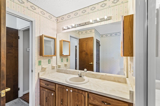 bathroom featuring wallpapered walls, a textured ceiling, and vanity