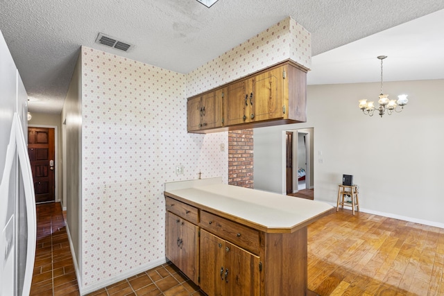 kitchen featuring a peninsula, a textured ceiling, visible vents, baseboards, and wallpapered walls