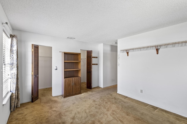unfurnished bedroom featuring a textured ceiling, a closet, a walk in closet, light carpet, and visible vents