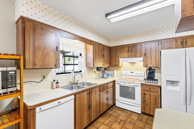 kitchen with wallpapered walls, under cabinet range hood, light countertops, a sink, and white appliances