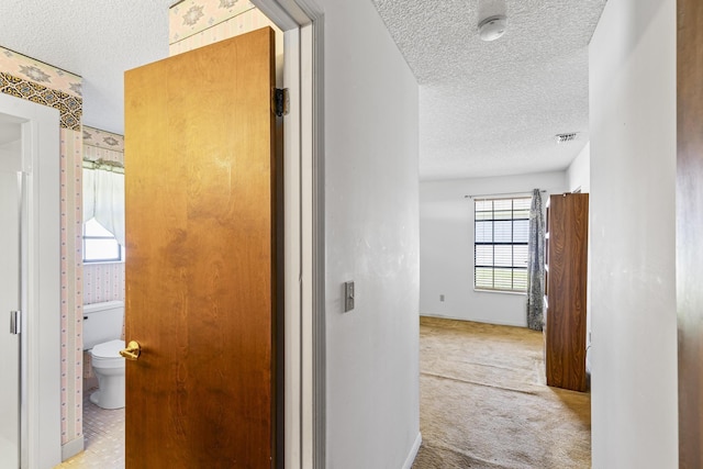 corridor with a textured ceiling, carpet flooring, baseboards, and visible vents