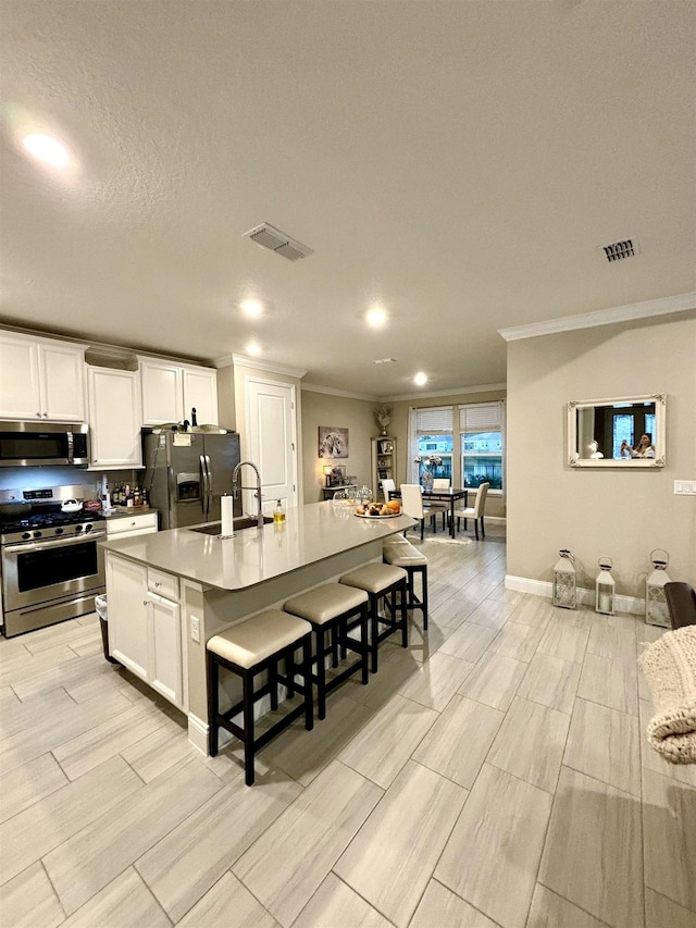 kitchen with white cabinetry, sink, stainless steel appliances, an island with sink, and a breakfast bar