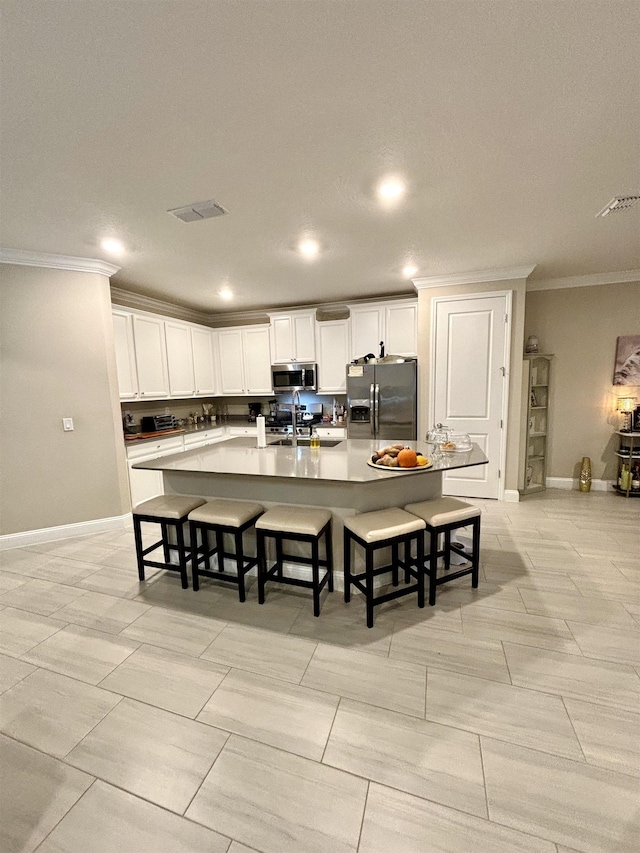 kitchen with white cabinetry, stainless steel appliances, crown molding, a breakfast bar, and a center island with sink