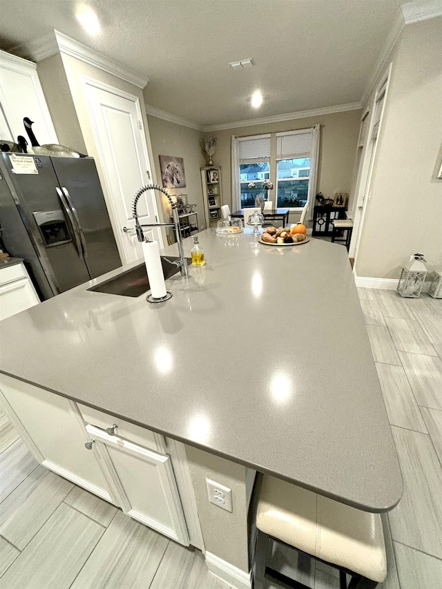 kitchen with white cabinetry, stainless steel fridge, sink, and crown molding