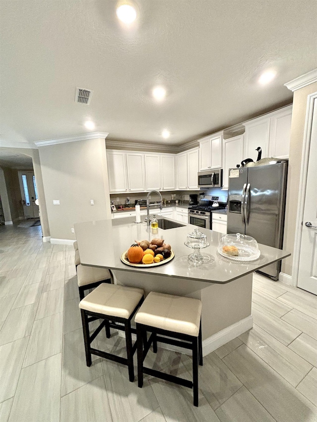 kitchen featuring a breakfast bar, stainless steel appliances, sink, a center island with sink, and white cabinetry