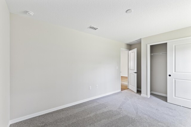 unfurnished bedroom featuring a textured ceiling, light carpet, and a closet