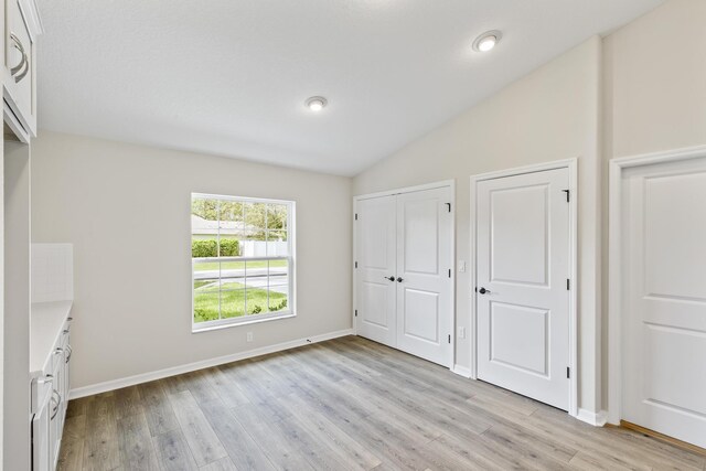 unfurnished bedroom featuring multiple closets, light wood-type flooring, and vaulted ceiling