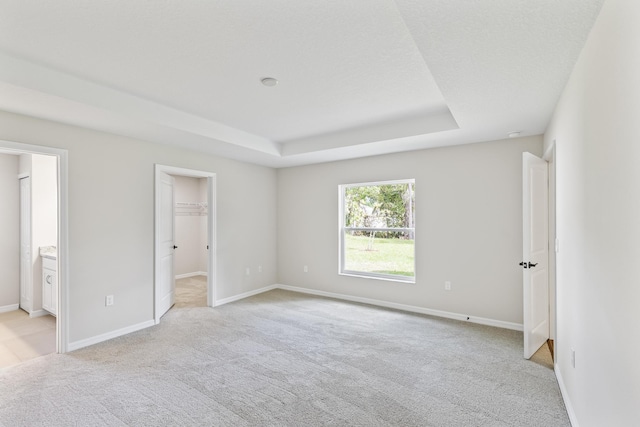 unfurnished bedroom featuring a raised ceiling, a walk in closet, connected bathroom, light colored carpet, and a closet