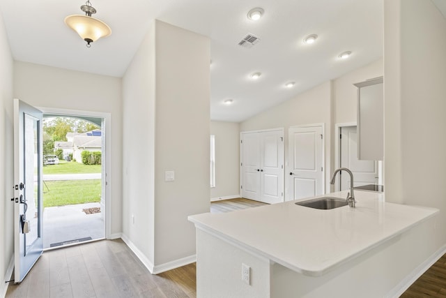 kitchen featuring kitchen peninsula, light wood-type flooring, vaulted ceiling, and sink