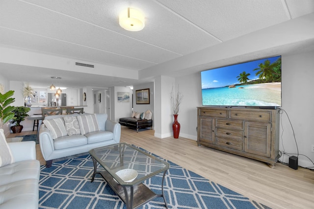 living area featuring visible vents, a textured ceiling, baseboards, and wood finished floors