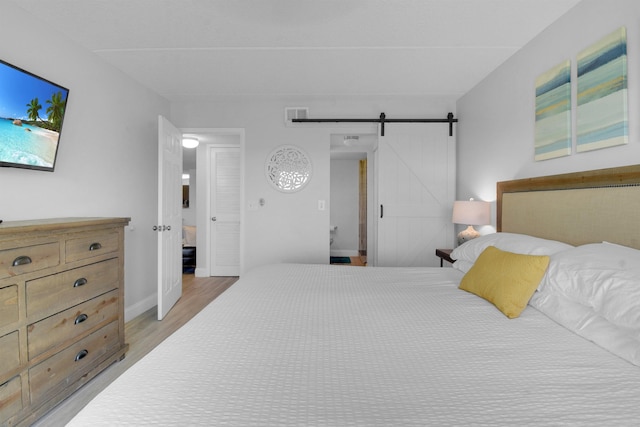 bedroom with light wood finished floors, a barn door, visible vents, and baseboards