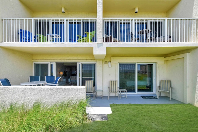 rear view of property with a patio, a lawn, a balcony, and stucco siding