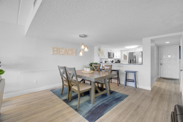 dining area with light wood-style flooring, baseboards, and a textured ceiling